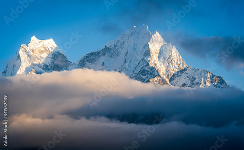 Thamserku and Kangtega peaks above clouds shining before the sunset. Thamserku (6623 meters high on the right) is a prominent peak you see during the Everest Base Camp trek in Nepal.  photo