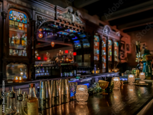 Old wooden bar counter with candles, bar tools and a blurred baroque or Victorian bar with bottles in the background
