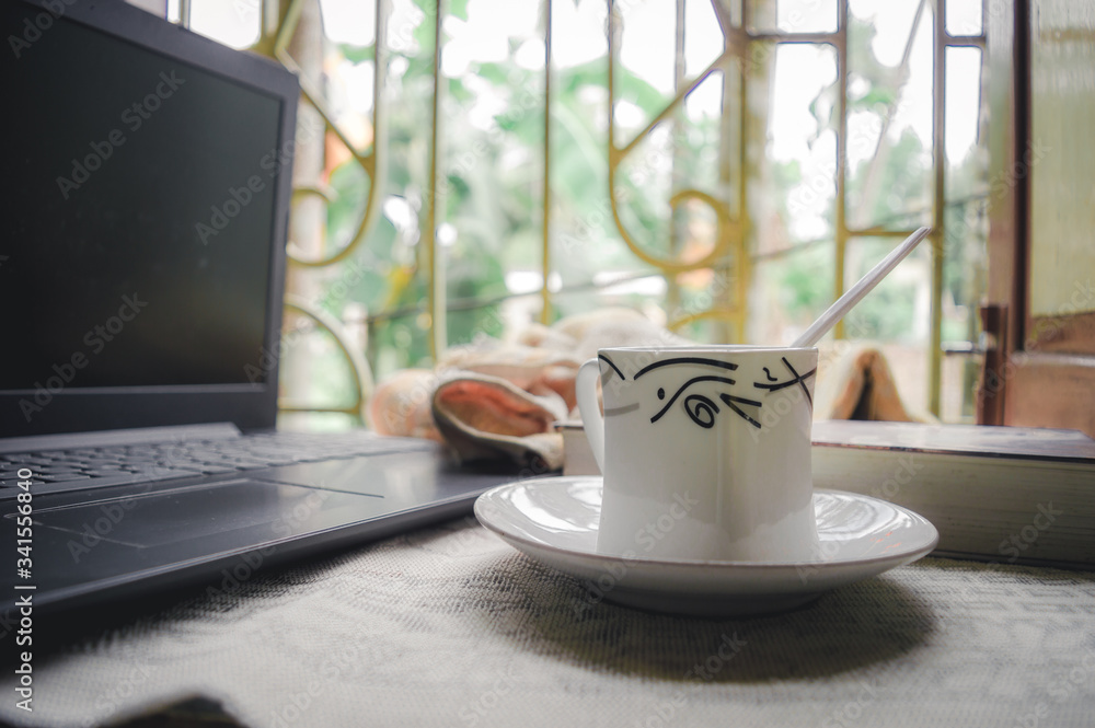 A cup of coffee a book and laptop on window sunlight in morning. A daily routine during social distancing period. Stay home, Work from home, Remote Work and Business Continuity background. A cup of coffee a book and laptop on window sunlight in morning. A daily routine during social distancing period. Stay home, Work from home, Remote Work and Business Continuity background.