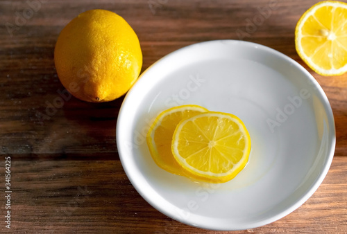 limón amarillo con cortes de limon en un plato de ceramica blanca vista desde arriba sobre una madera