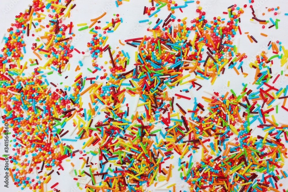 confectionery powder for decorating cupcakes and cakes. Decorative sprinkles border on white background. Multicolor Sugar confectionery powder in the corner. Scattered sweet sugar sticks and balls.