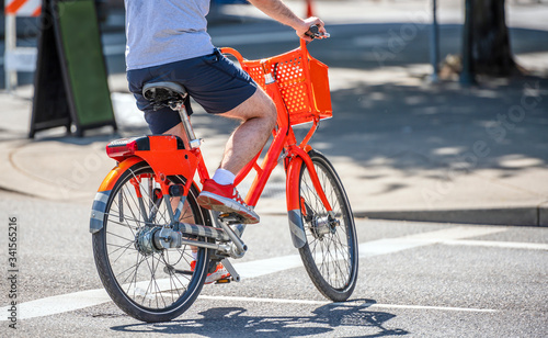Man takes a ride on a rented orange bicycle with a basket preferring an active lifestyle that is healthy