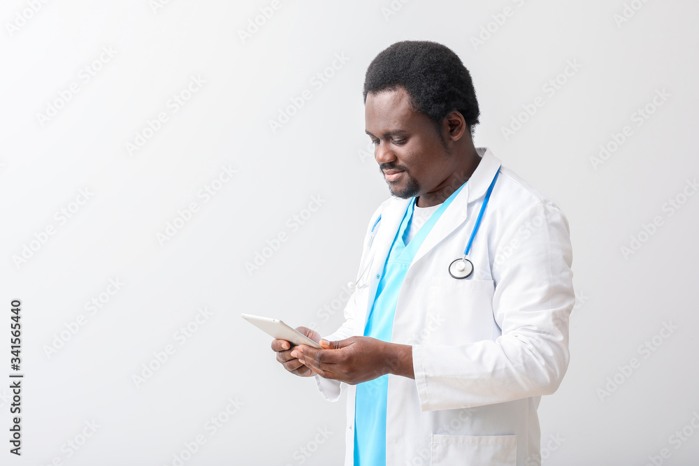Male African-American doctor with tablet computer on light background Male African-American doctor with tablet computer on light background