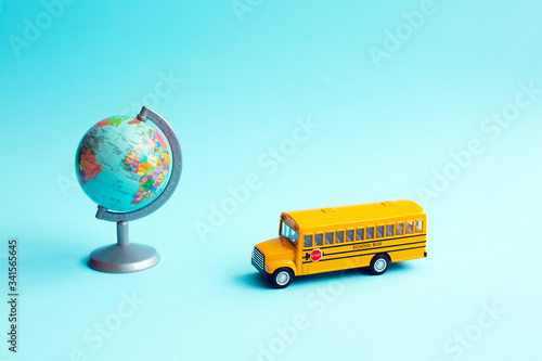 Yellow school bus toy near to globe on blue background.