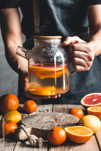 A man pours citrus tea on a wooden table. Healthy drink, vintage style. Vegan, eco products.