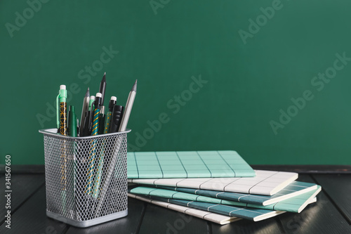 Holder with stationery on table near blackboard