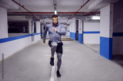 Young muscular sportsman running in place and warming up in underground garage.