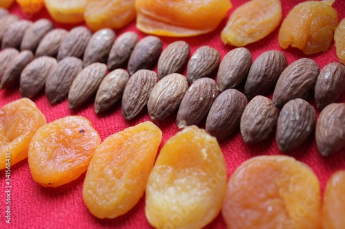 Obraz na płótnie Almonds and dried apricots lined with a line on a red background. Almonds and dried apricots close-up with place for text. Nuts and dried fruits, healthy nutrition. w salonie