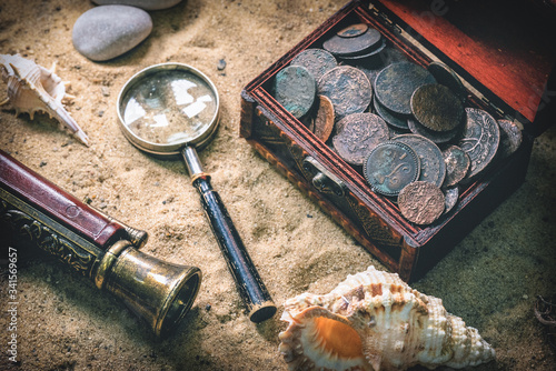 Pirate treasure chest with ancient coins and other various pirate equipment on flat lay table background.