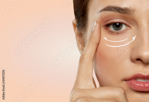 beauty, makeup and lifting concept - close up of beautiful young woman face with arrows under eye area over beige background