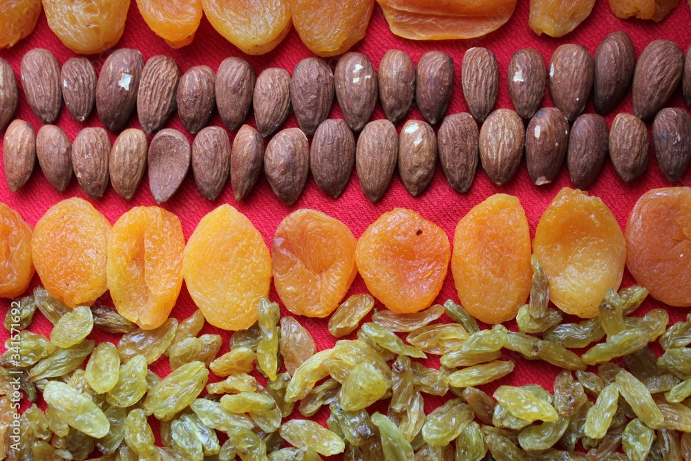 Assortment of nuts,dried fruits and seeds on a wood background.Dried fruits and nuts, symbols of judaic holiday Tu Bishvat. Almonds, raisins and dried apricots laid out by a line on a red background.