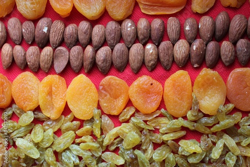 Obraz na płótnie Assortment of nuts,dried fruits and seeds on a wood background.Dried fruits and nuts, symbols of judaic holiday Tu Bishvat. Almonds, raisins and dried apricots laid out by a line on a red background. w salonie
