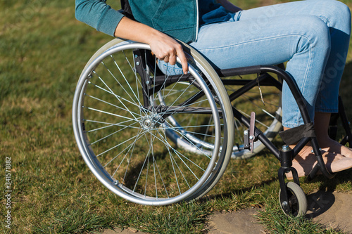 Close up of a young woman in a wheelchair while walking in a park on a sunny day. Recovery and healthcare concepts.