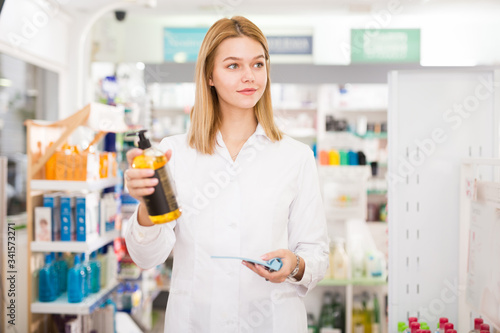 Portrait of smiling pleasant positive female druggist in white coat working in pharmacy