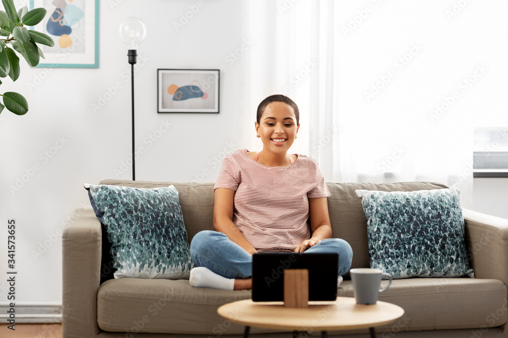 people, technology and leisure concept - happy young african american woman sitting on sofa with tablet pc computer and watching movie at home people, technology and leisure concept - happy young african american woman sitting on sofa with tablet pc computer and watching movie at home