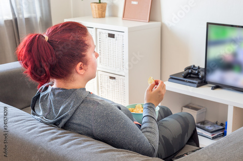 Middle age woman relaxing on the sofa, watching TV and eating chips, closeup