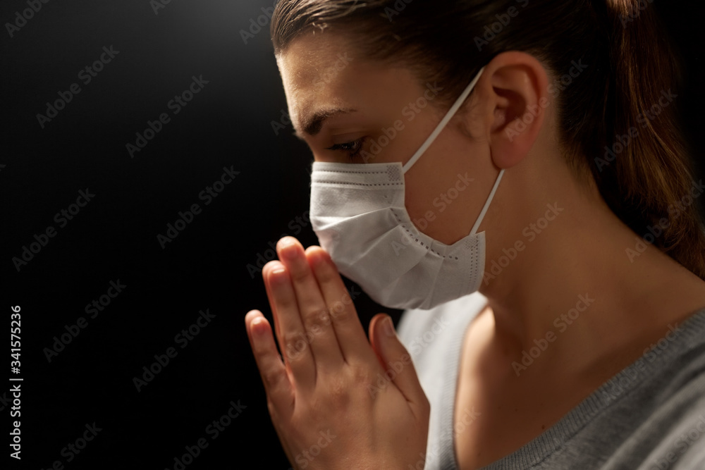 health protection, safety and pandemic concept - close up of sick young woman in protective medical face mask praying over black background