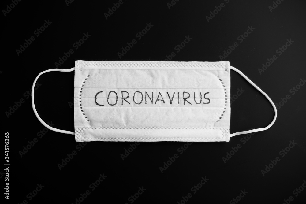 medicine, healthcare and safety concept - close up of white face protective medical mask with coronavirus word on it on black background medicine, healthcare and safety concept - close up of white face protective medical mask with coronavirus word on it on black background