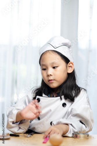 Happy Asian girl in chef uniform playing at home.