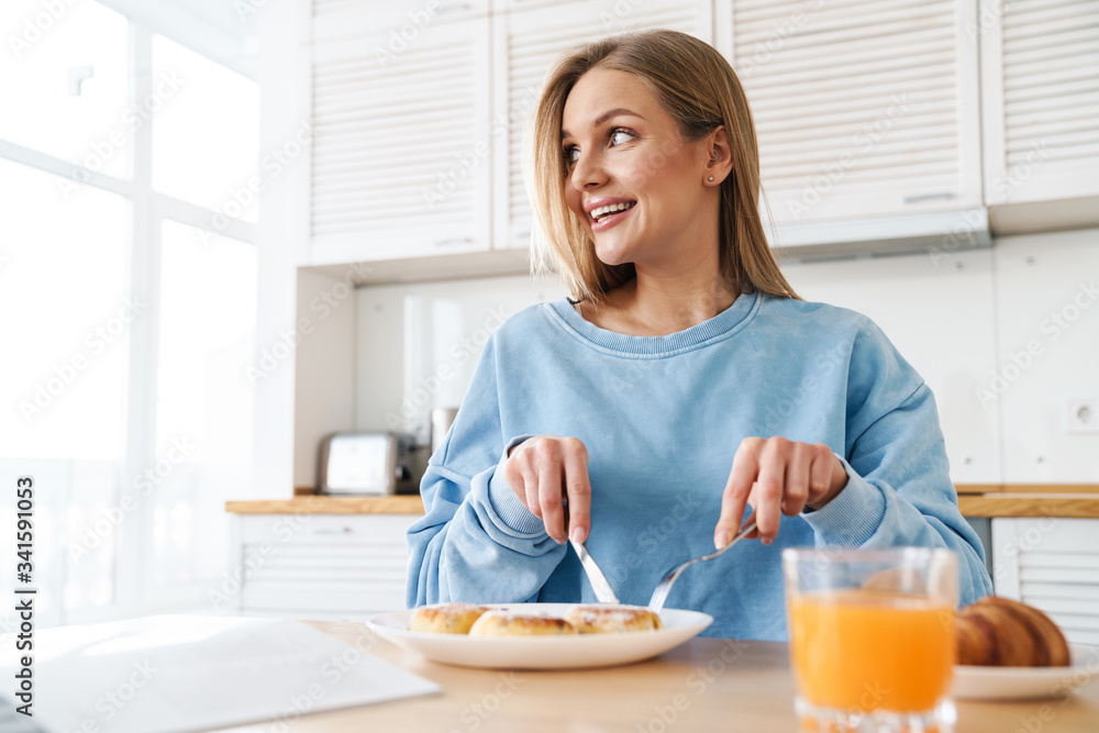 Image of cheerful young woman smiling while having breakfast Image of cheerful young woman smiling while having breakfast