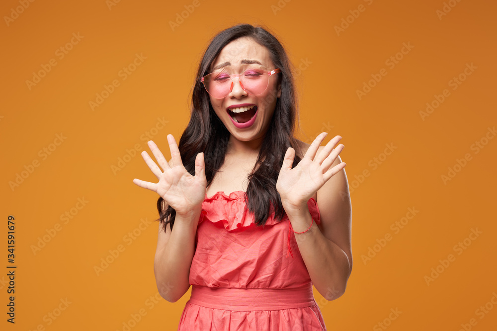 Screaming asian girl in pink glasses on empty orange background Screaming asian girl in pink glasses on empty orange background