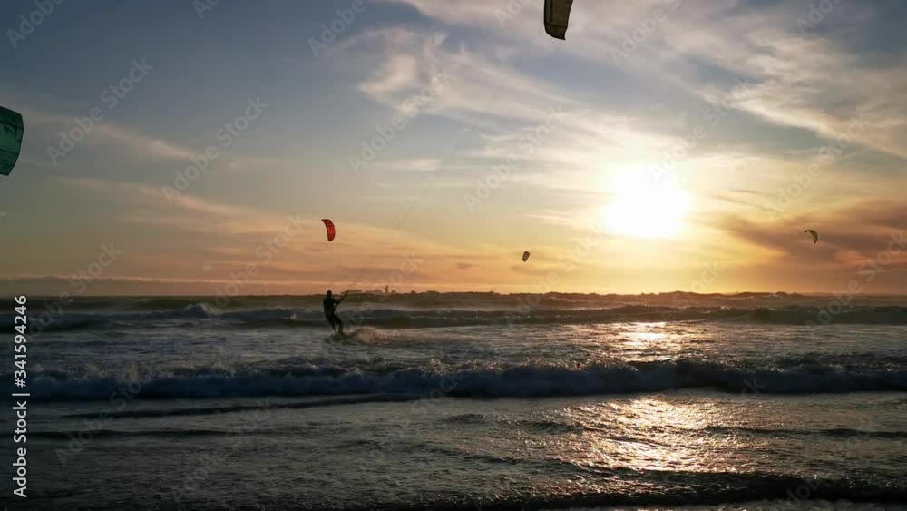 Male kitesurfer in ocean environment along with other kitesurfers.