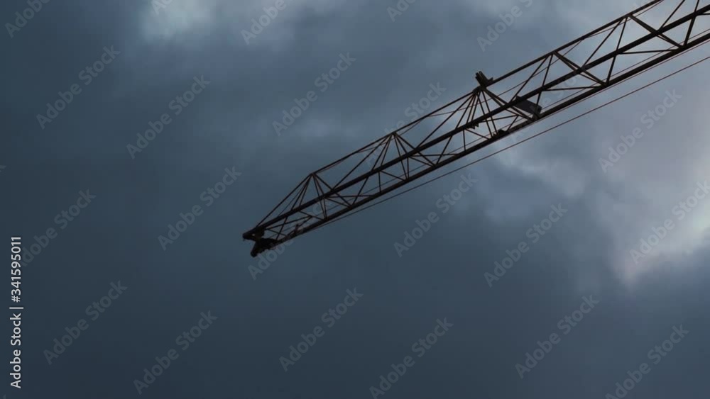 A tall construction crane stopped and in the background a dark colored cloudy sky A tall construction crane stopped and in the background a dark colored cloudy sky