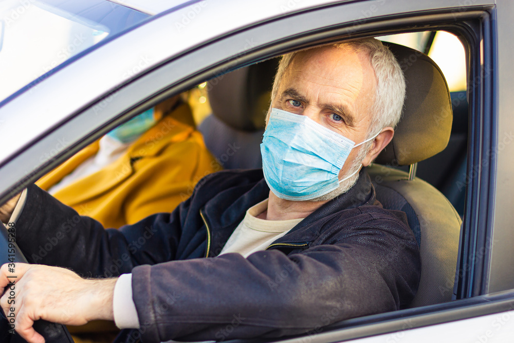 Senior man in a medical face mask driving a car. Coronavirus pandemic concept. Road trip, travel and old people concept - happy senior couple driving in car Senior man in a medical face mask driving a car. Coronavirus pandemic concept. Road trip, travel and old people concept - happy senior couple driving in car