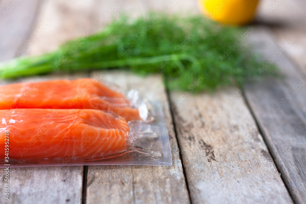 Red fish o salmon fillets in vacuum package on wooden background. Fresh fish, lemon and dill for cooking ingredients. Concept of healthy eating. Omega-3. Selective focus. Close up. Copy space Red fish o salmon fillets in vacuum package on wooden background. Fresh fish, lemon and dill for cooking ingredients. Concept of healthy eating. Omega-3. Selective focus. Close up. Copy space