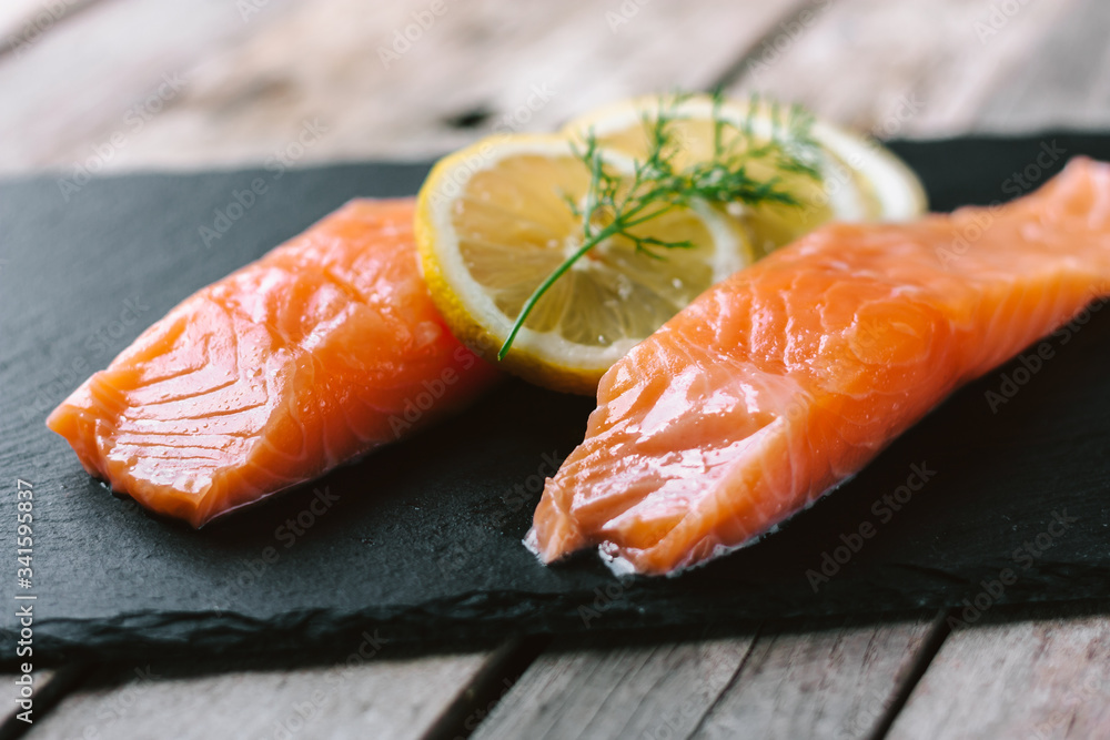 Red fish o salmon fillets on stone slate on wooden background. Fresh fish, lemon and dill for cooking ingredients. Concept of healthy eating. Omega-3. Close up. Red fish o salmon fillets on stone slate on wooden background. Fresh fish, lemon and dill for cooking ingredients. Concept of healthy eating. Omega-3. Close up.