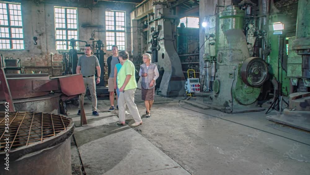 Family of four takes tour in old steel mill with industrial machines. The guide explains the gigantic machines. Slow Motion Tracking shot. Family of four takes tour in old steel mill with industrial machines. The guide explains the gigantic machines. Slow Motion Tracking shot.