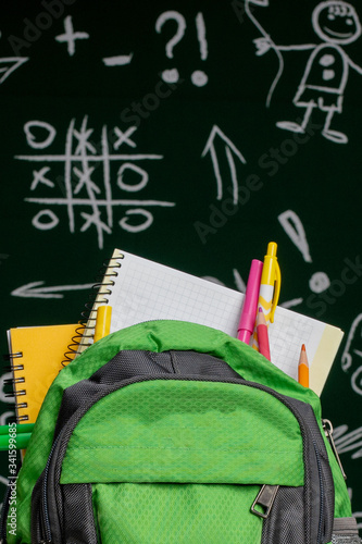 Education concept - green backpack  notebooks and school supplies on the background of the blackboard