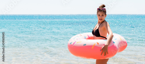 Shocked young woman inside donut rubber ring is standing in the cold water