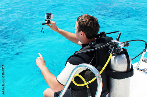 Happy scuba diver with equipment and camera is preparing for his diving lesson in the blue sea