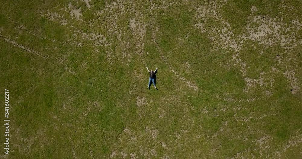Aerial drone shot of flying up over the adult woman wearing a black t-shirt lying on the green grass at the park. Aerial drone shot of flying up over the adult woman wearing a black t-shirt lying on the green grass at the park.