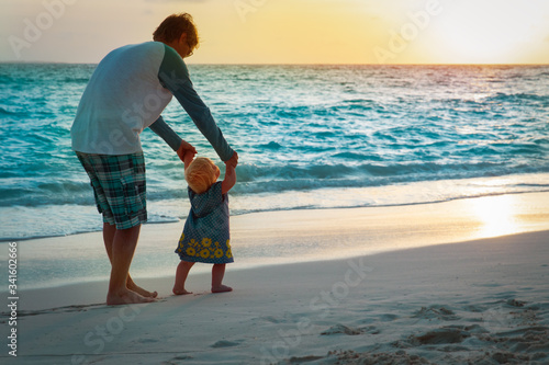 father and little daughter making first steps on sunset beach