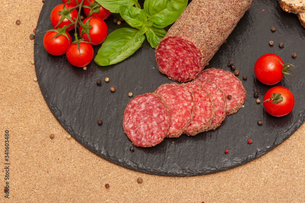 sliced smoked sausage with sauce, cherry tomatoes and basil on a black graphite board with slices of bread. top view sliced smoked sausage with sauce, cherry tomatoes and basil on a black graphite board with slices of bread. top view