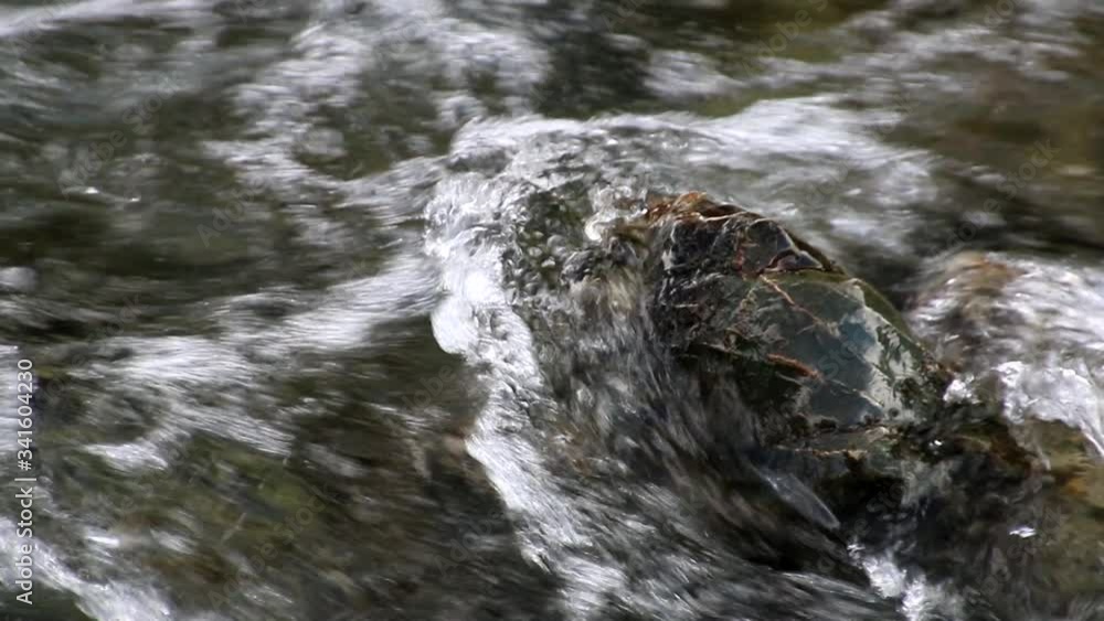 A close up of a river rock protruding out of the rocky river bottom of a fast moving wild and scenic river and being washed over by the clear water. A close up of a river rock protruding out of the rocky river bottom of a fast moving wild and scenic river and being washed over by the clear water.