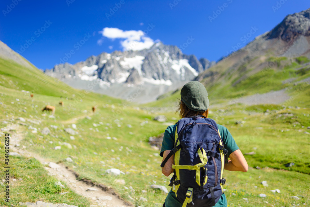 Woman with backpack hiking towards mountain top, scenic glacier and dramatic landscape summer fitness wellbeing selective focus rear view, freedom concept