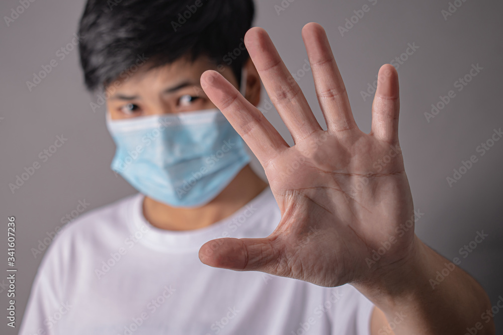 Closeup of a man wearing a protective mask and stop hands on a gray background. Closeup of a man wearing a protective mask and stop hands on a gray background.