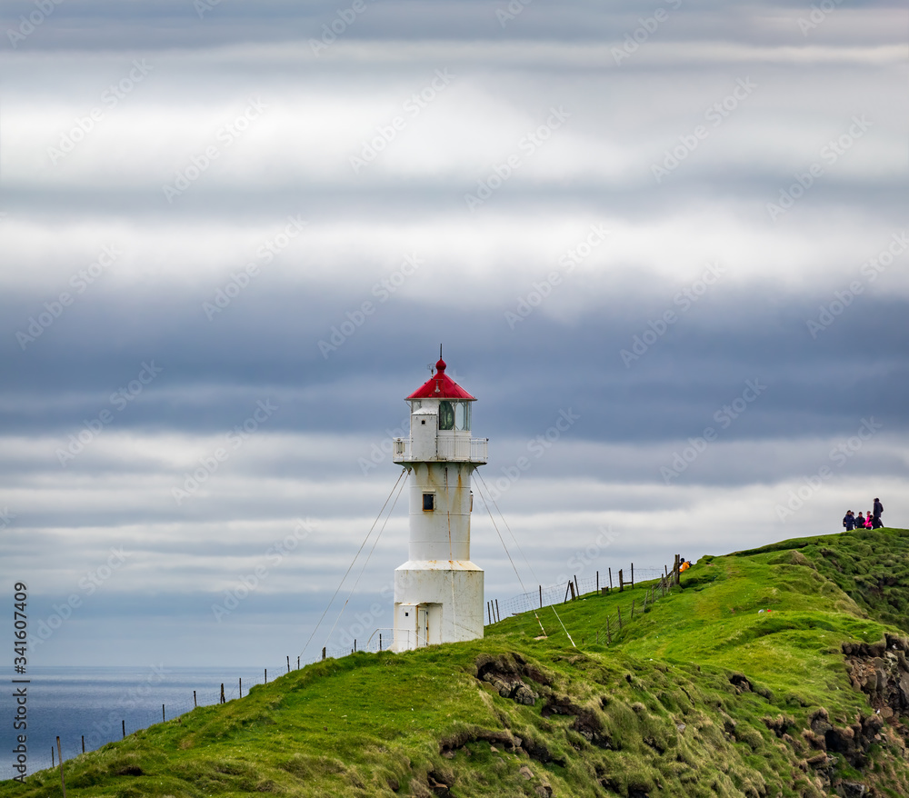 Lighthouse with red cap under the cloudy sky with tourists
