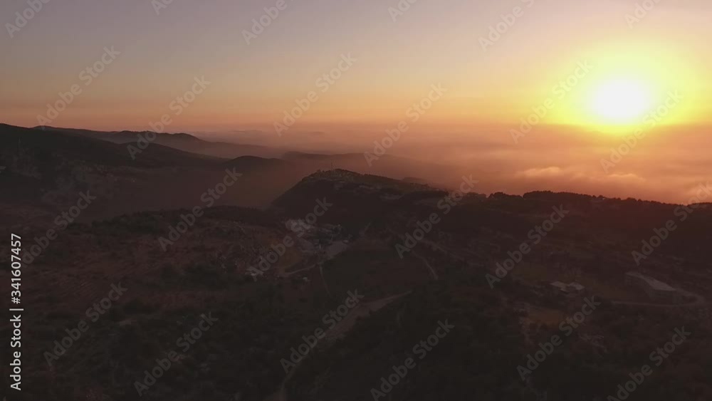 Stunning high aerial view above mountain range and clouds toward bright yellow sunset Stunning high aerial view above mountain range and clouds toward bright yellow sunset