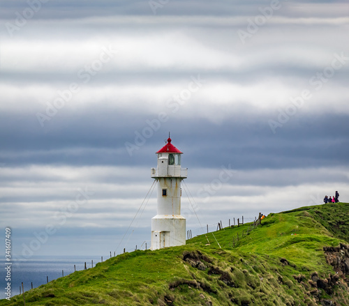 Lighthouse with red cap under the cloudy sky with tourists