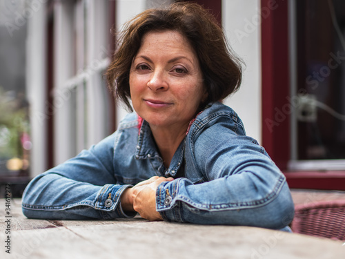 Portrait of senior pensive lady, sitting in cafe and looking at camera. Street scene, daily life.