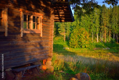 An old traditional rustic wooden house (log cabin) with a small windows. Green birch tree forest in the background. Pastoral landscape. Setomaa, Estonia photo