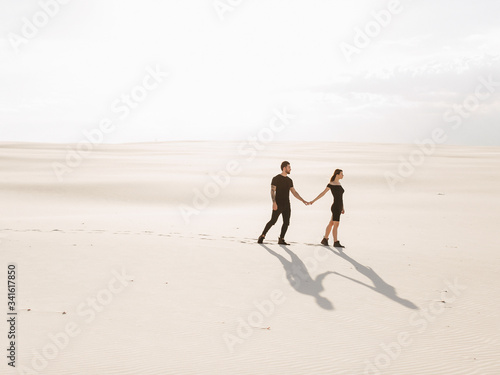 Lovely attractive couple on the white sand beach or in the desert or in the sand dunes. Beach honeymoon couple holding hands walking on white sand beach 