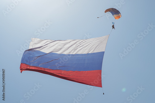 Skydiver in the sky with a giant flag of Russia against the blue sky.