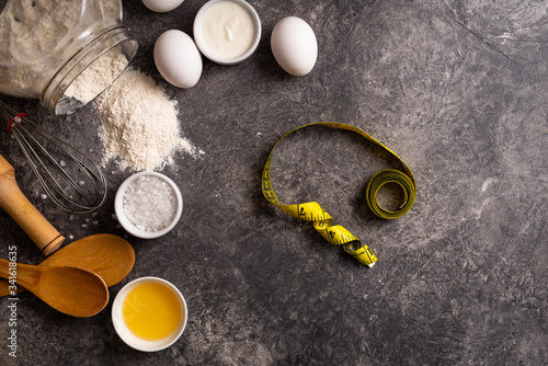 Ingredients for making healthy dough, flour, eggs, sea salt, sour cream on a stone background with a centimeter tape. Top view, copy space.
