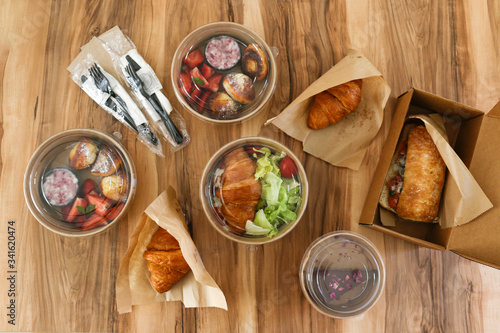 Different takeout food on wooden kitchen table. Italian panini sandwich, french croissant with salmon, strawberry pancakes and chocolate cheesecake. Close up, top view, pov, copy space, background.