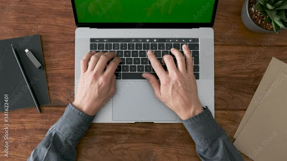 Top view of young white male hands typing on modern space grey laptop computer on a rustic wooden desk.